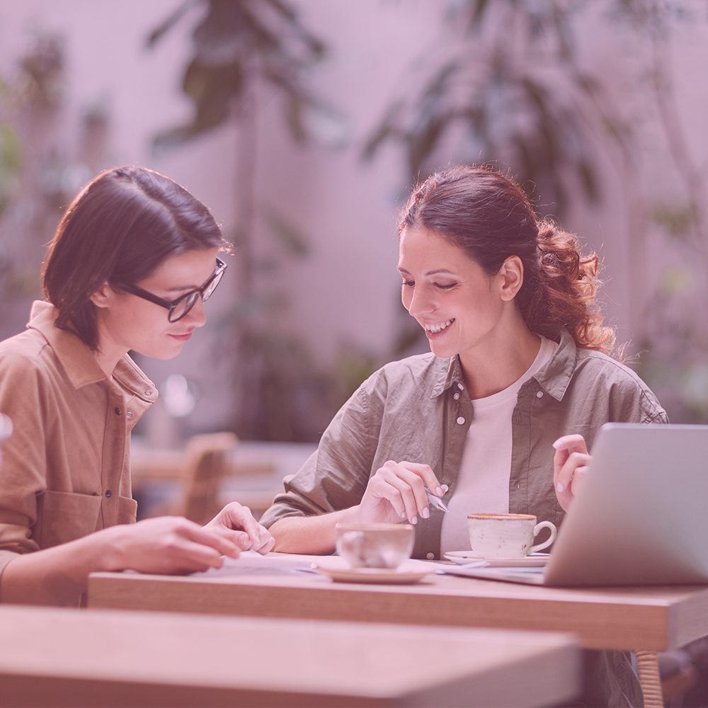 Zwei Frauen arbeiten zusammen an einem Dokument | lächelnd | Café