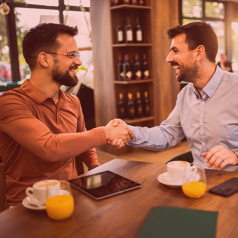 Zwei Männer reichen sich die Hand | lächelnd | Café